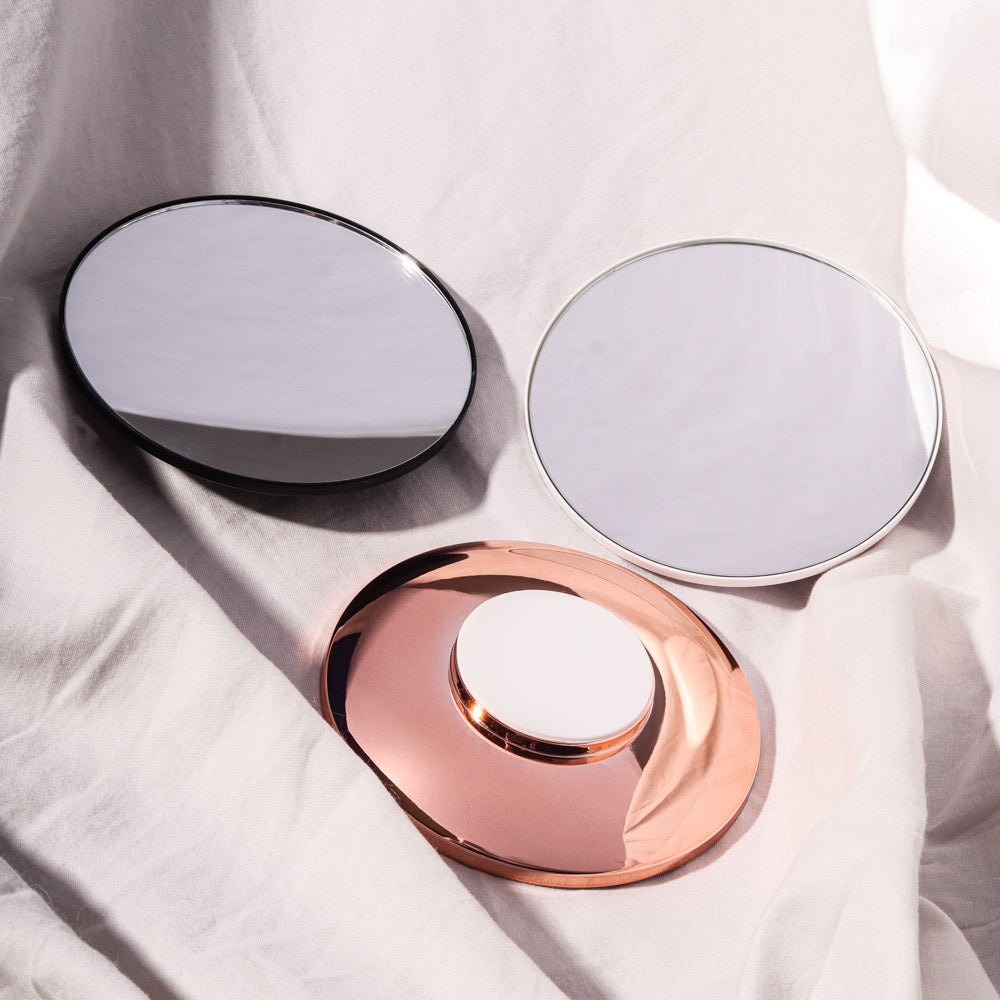 Three Lara 10x magnifying mirror attachments for the Vera mirror in black, white, and rose gold on white fabric.