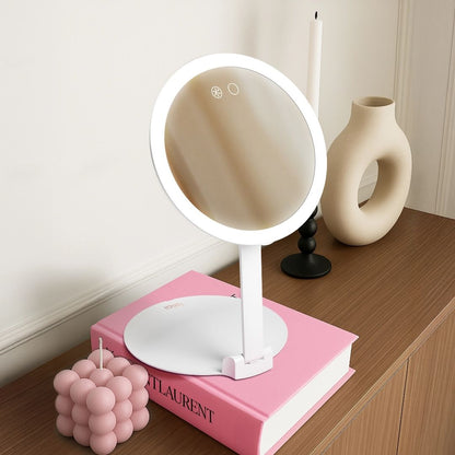 Abigail LED travel mirror with 10x magnification and adjustable stand on a vanity with pink book and decor.