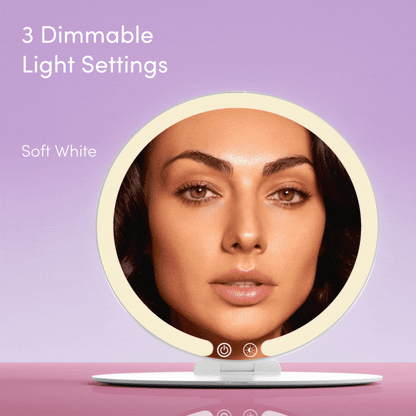 Abigail LED travel mirror with dimmable soft white light setting reflecting a woman's face on a purple background.