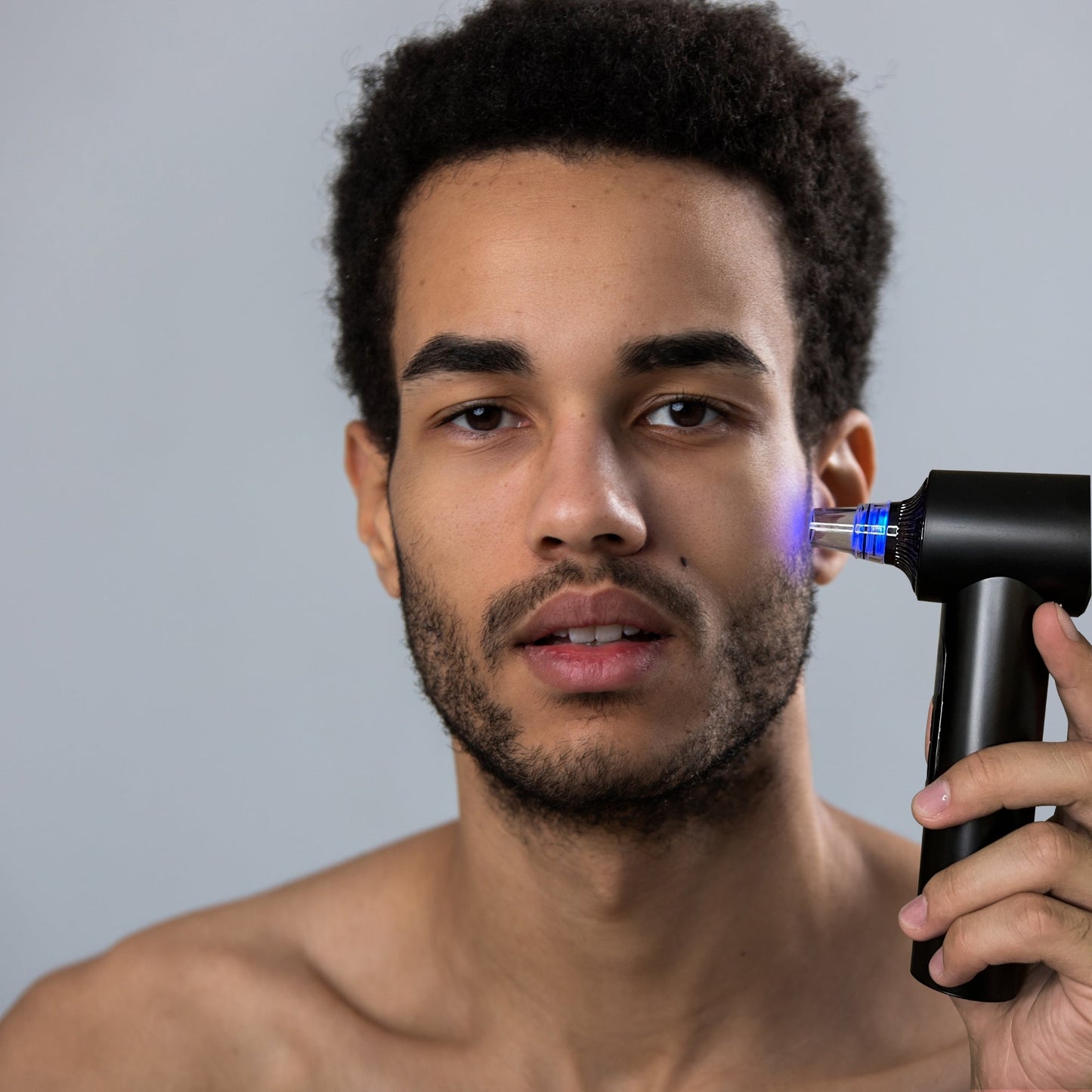 Man using Clara Microdermabrasion device with blue LED light on cheek for pore vacuuming and blackhead removal.