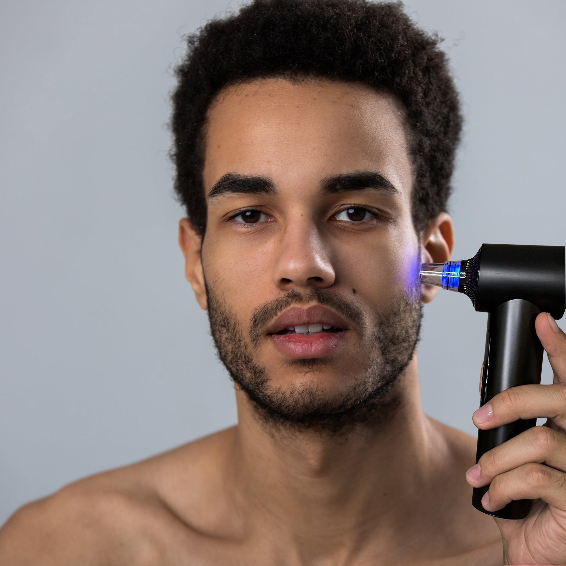 Man using Clara Microdermabrasion device with blue LED light on cheek for pore vacuuming and blackhead removal.