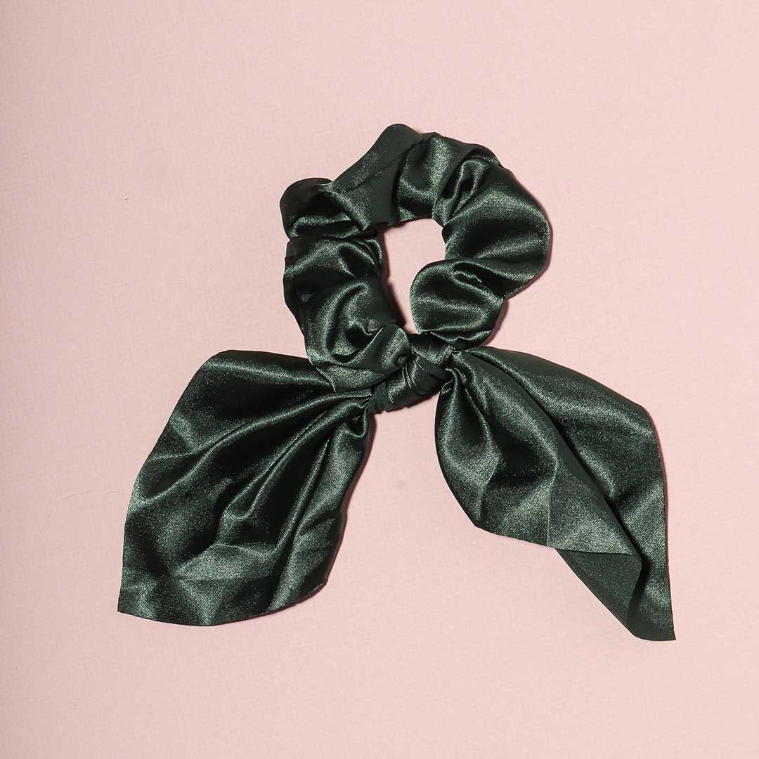 Elle dark green satin scrunchie with a chic bow attachment, displayed flat on a light pink background.