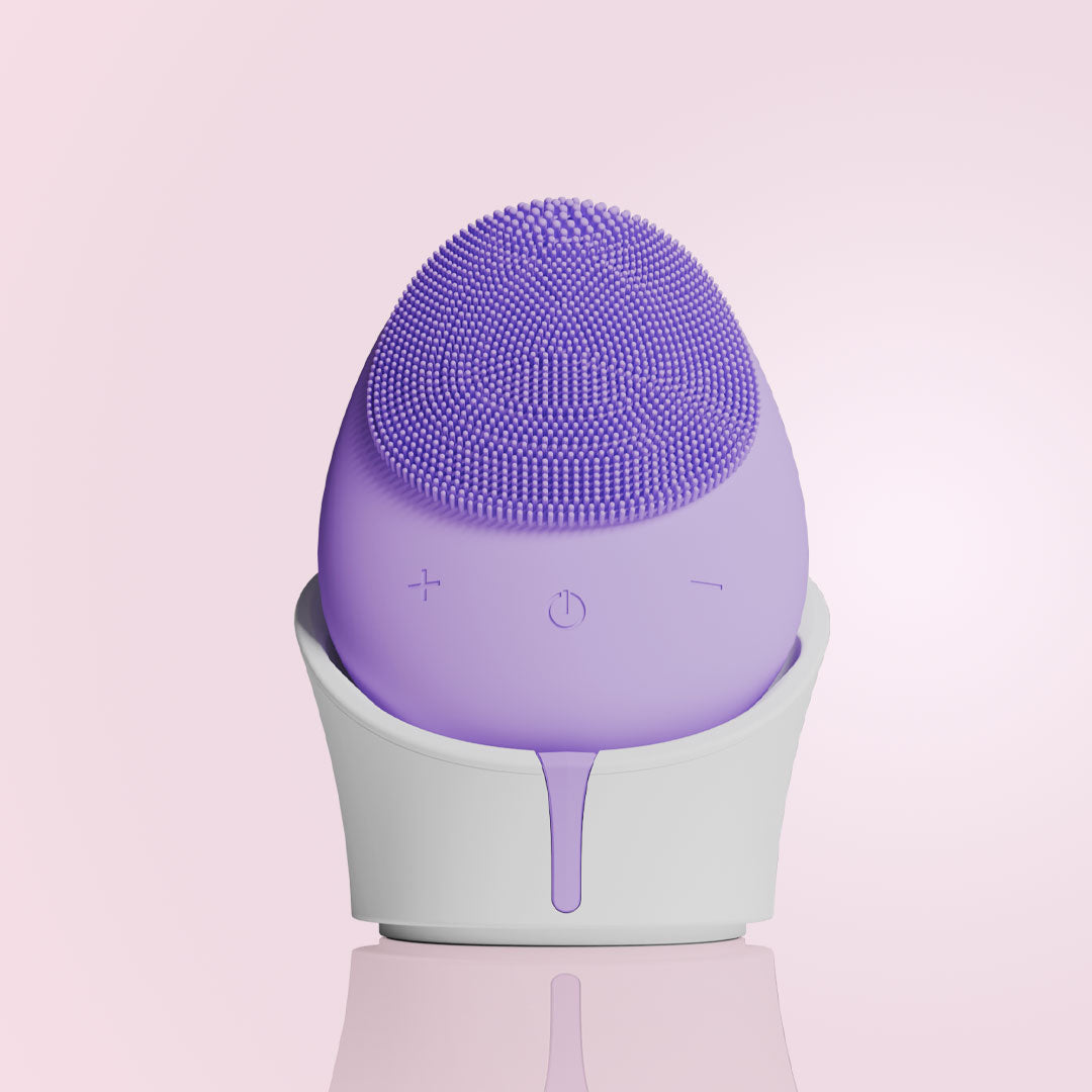 Purple Isla sonic facial cleansing brush with silicone bristles in a white charging base for exfoliating skincare.