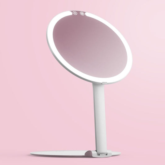 White Abigail LED travel makeup mirror with ring light and adjustable stand on a pink background.