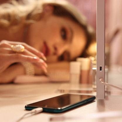 Side view of Monroe lighted vanity mirror with built-in USB charging port powering a smartphone on a makeup desk.