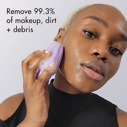 A woman uses the purple Isla sonic facial cleansing brush to gently exfoliate and remove dirt from her glowing skin.