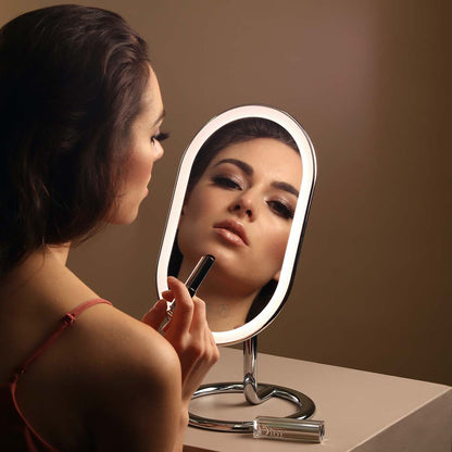 Vera Lighted Vanity Mirror with LED halo ring light and aluminum stand, used by a woman applying makeup.