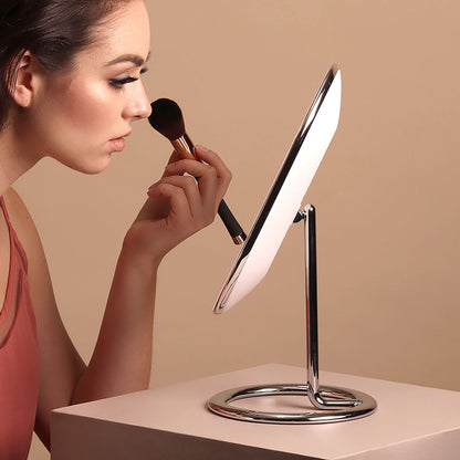 Woman applying makeup with a brush using the Vera Lighted Vanity Mirror in sleek chrome aluminum finish.