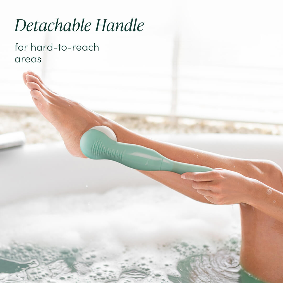 Cora 7 electric body cleansing brush with detachable long handle used to exfoliate legs in a bubble bath.