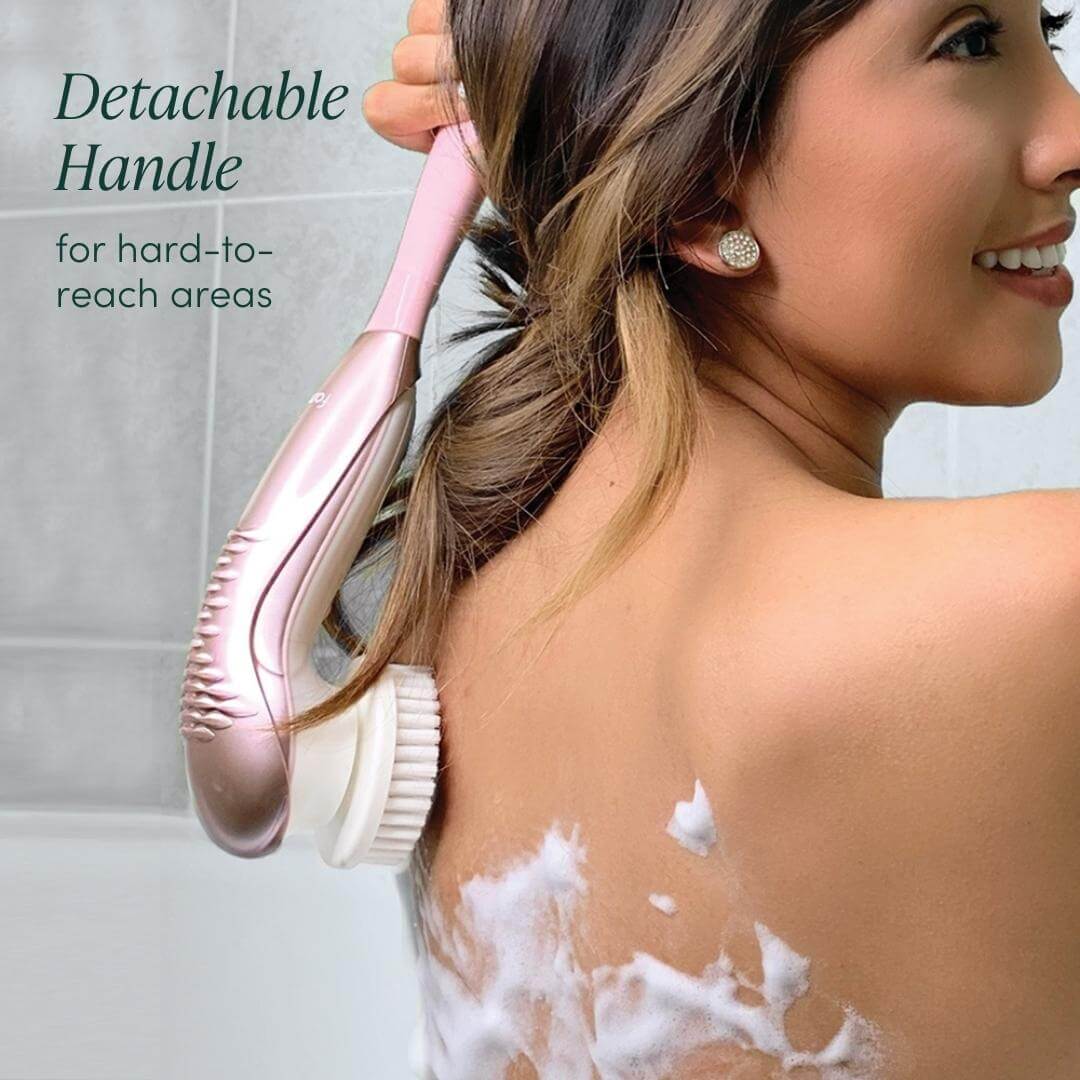 Woman using the Cora 7 pink electric body cleansing brush with its detachable handle to exfoliate her back in the shower.