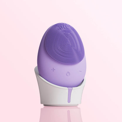 Isla purple silicone sonic facial cleansing brush with exfoliating bristles on a white charging stand.