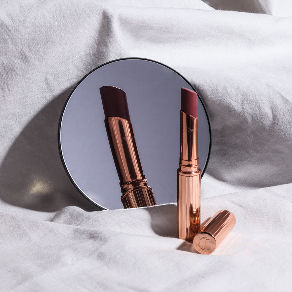 Lara 10x magnifying mirror for Vera reflecting a gold lipstick tube on a soft white fabric background.
