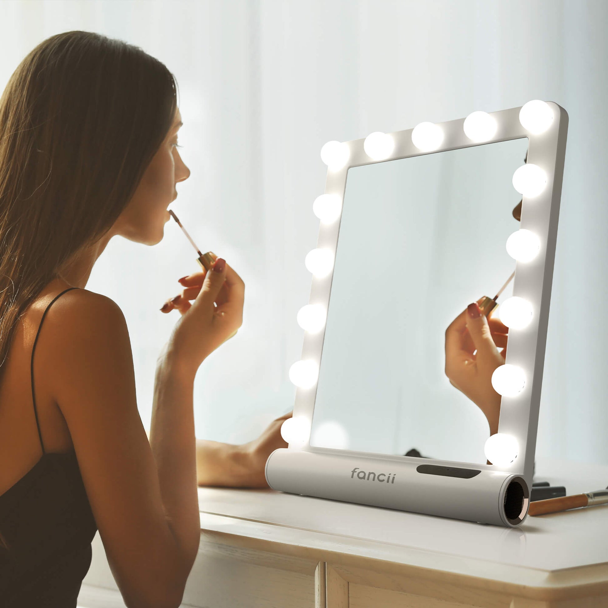 Madeline Mini Hollywood Mirror with LED bulbs and Bluetooth speaker used by a woman applying makeup at a vanity.