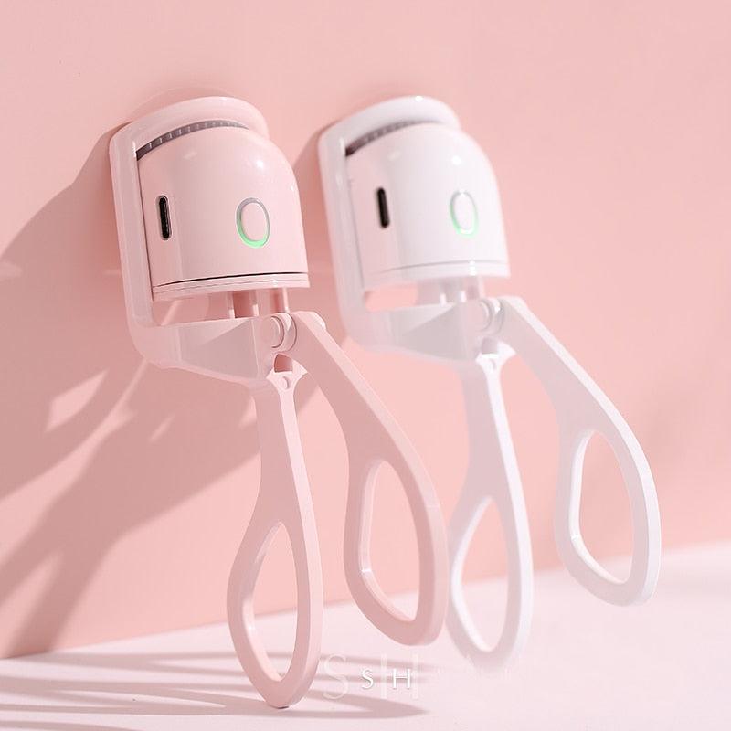 Pink and white LashWave electric heated eyelash curlers with USB charging ports against a soft pink background.