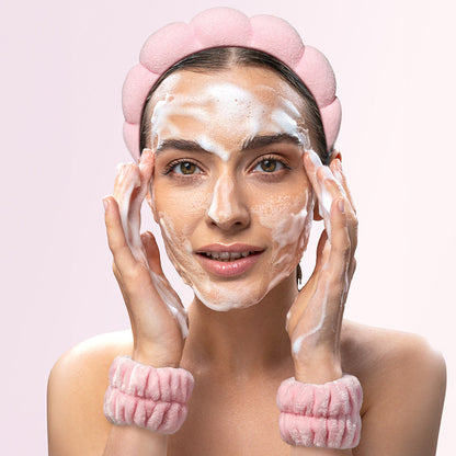 A woman washing her face with foam, wearing the pink Avery bubble spa headband and matching microfiber wristbands.
