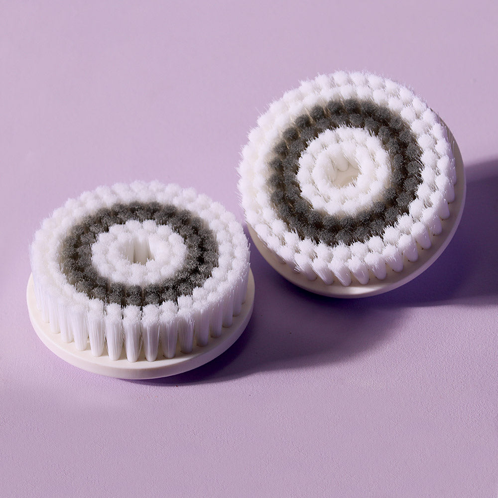 2-pack of Louvrs Cora Replacement Facial Cleansing Brush Heads with white and grey bristles on a purple background.