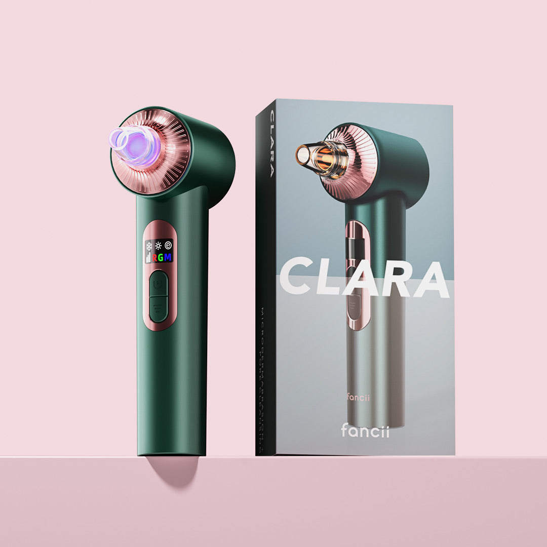 Clara Microdermabrasion Device and Pore Vacuum in emerald green next to its retail box on a pink background.