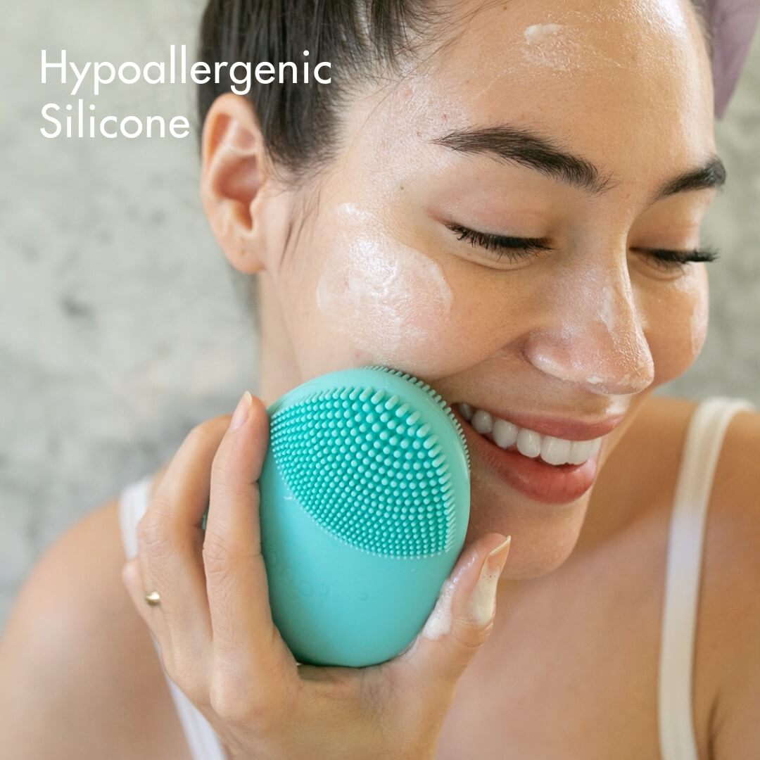 Woman using the Isla teal hypoallergenic silicone sonic facial cleansing brush to gently exfoliate for radiant skin.