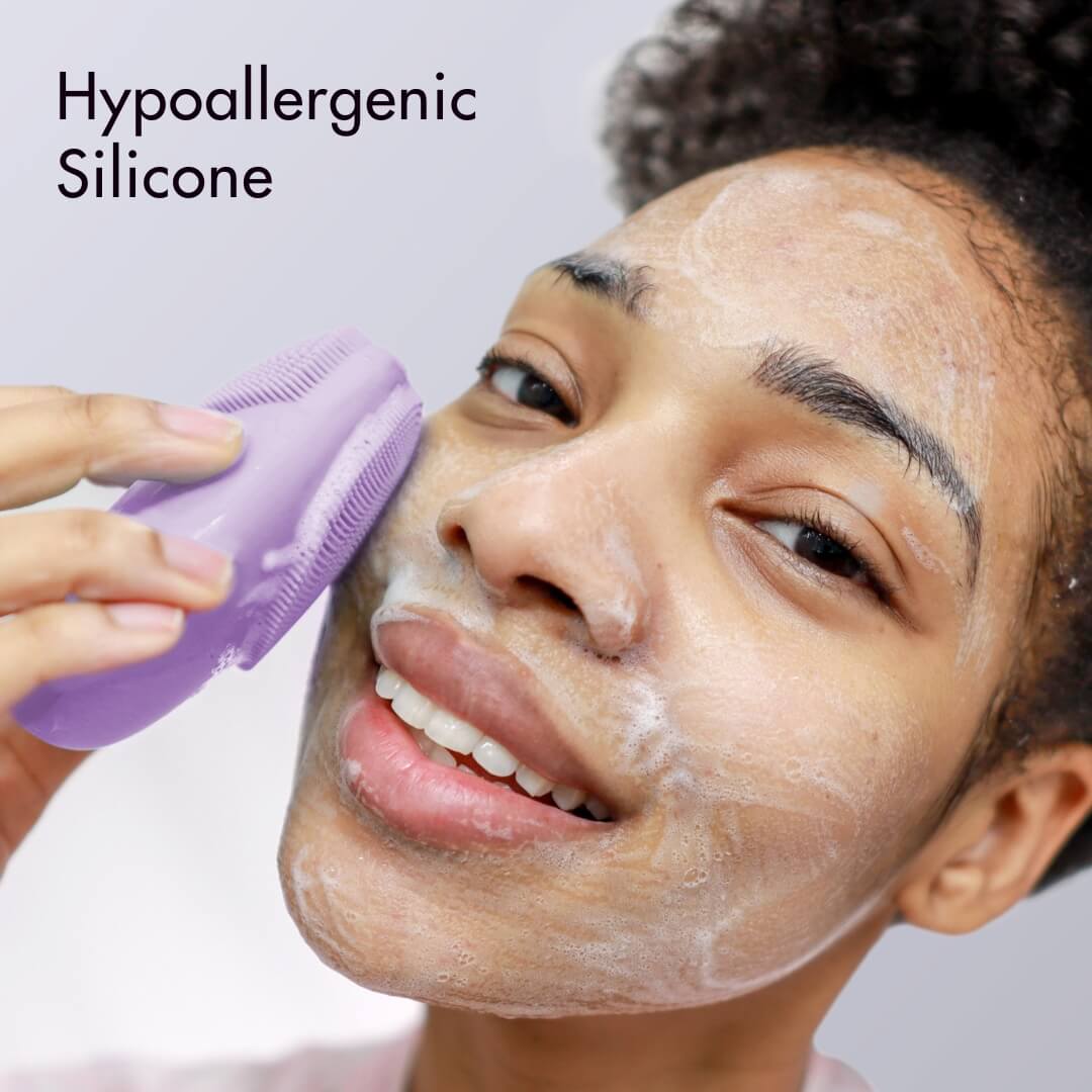 Isla purple hypoallergenic silicone sonic facial cleansing brush used by a smiling woman to exfoliate skin.