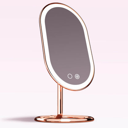 Vera rose gold lighted vanity mirror with LED ring light, tilting oval design, and touch sensors on a sturdy base.